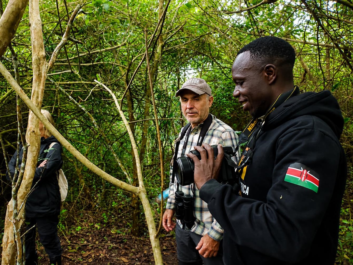 Francis Angara tours guide explaining a bird species to Premium eco-tourists during birdwatching and exploring the boardwalk trail at Bigodi Wetland Sanctuary operated by BICOWA near Kibale National Park Uganda.